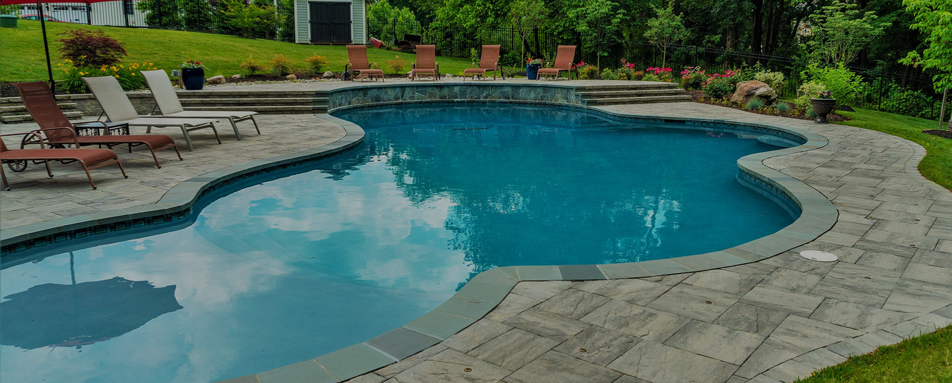 Freeform swimming pool with stone paving, pool cover prices guide