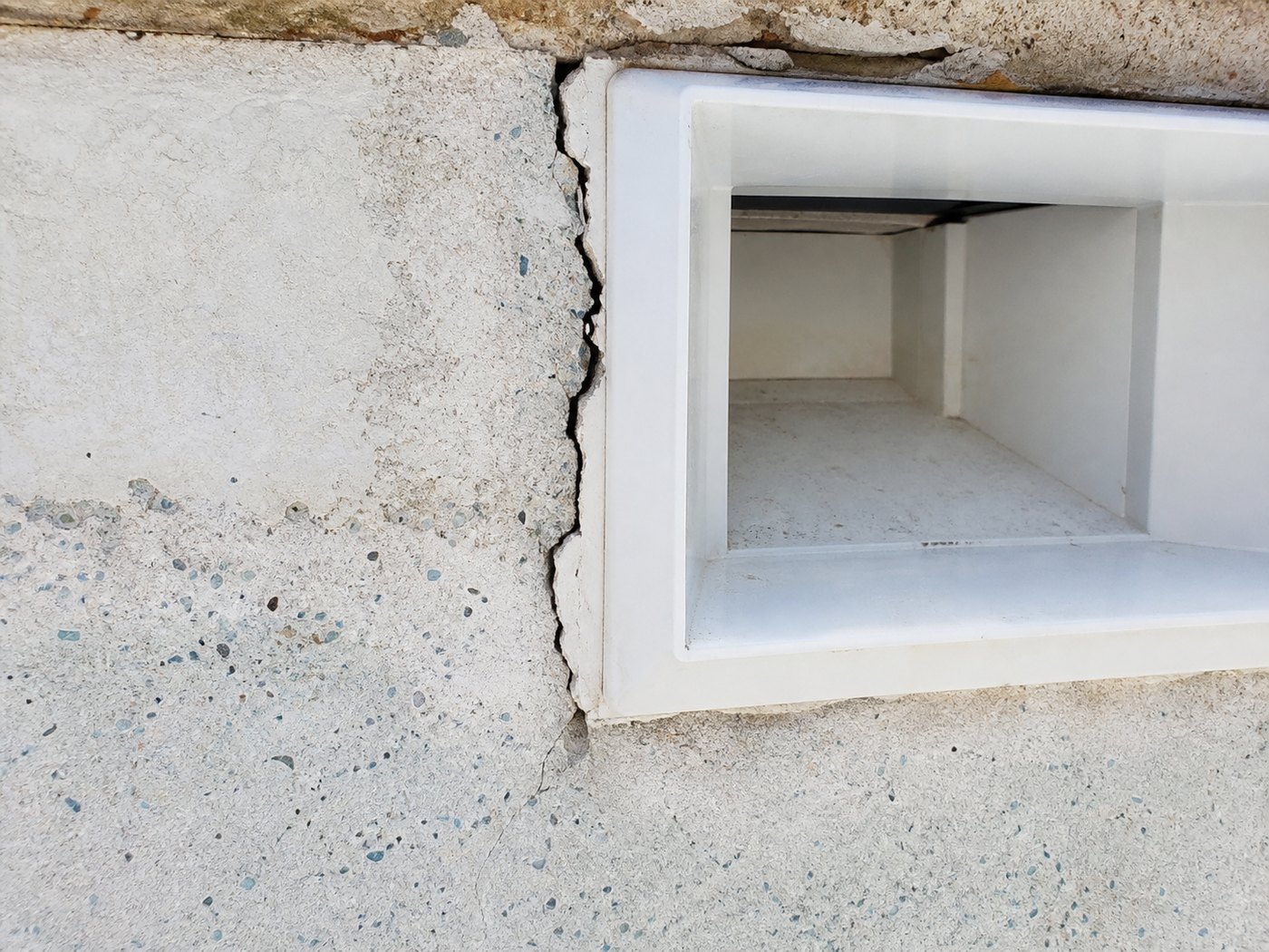Close-up of a cracked swimming pool skimmer weir where the plastic housing meets the pool shell, a common cause of water loss