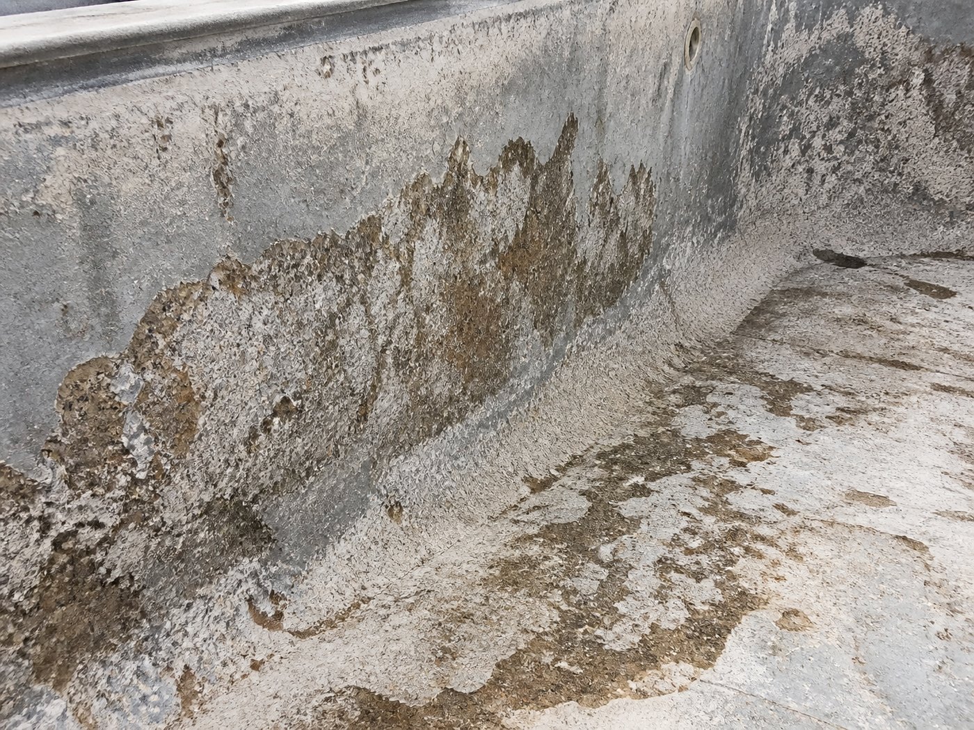 Chalky pitted grey marbelite pool surface with exposed aggregate and brown staining in an empty pool