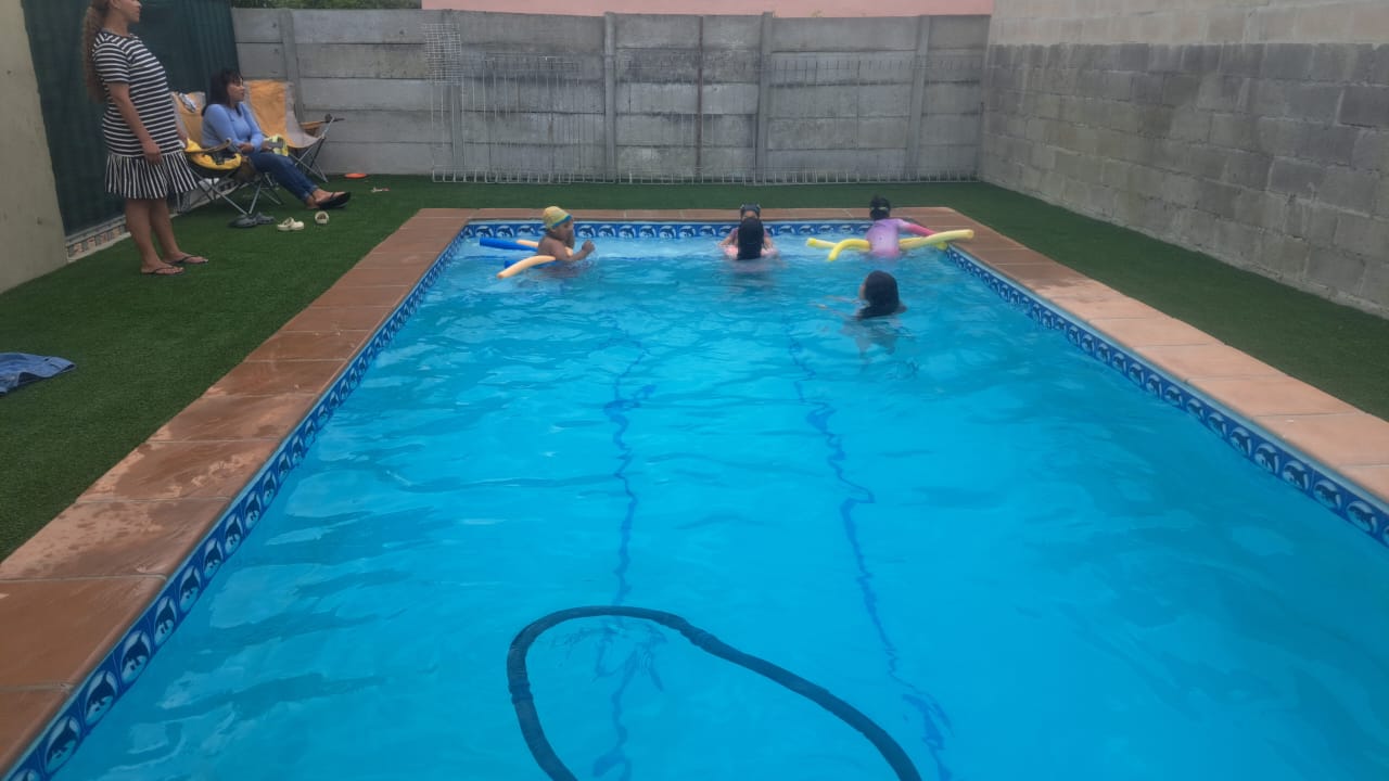 A finished rectangular pool with blue mosaic tiling and artificial lawn, with a family swimming