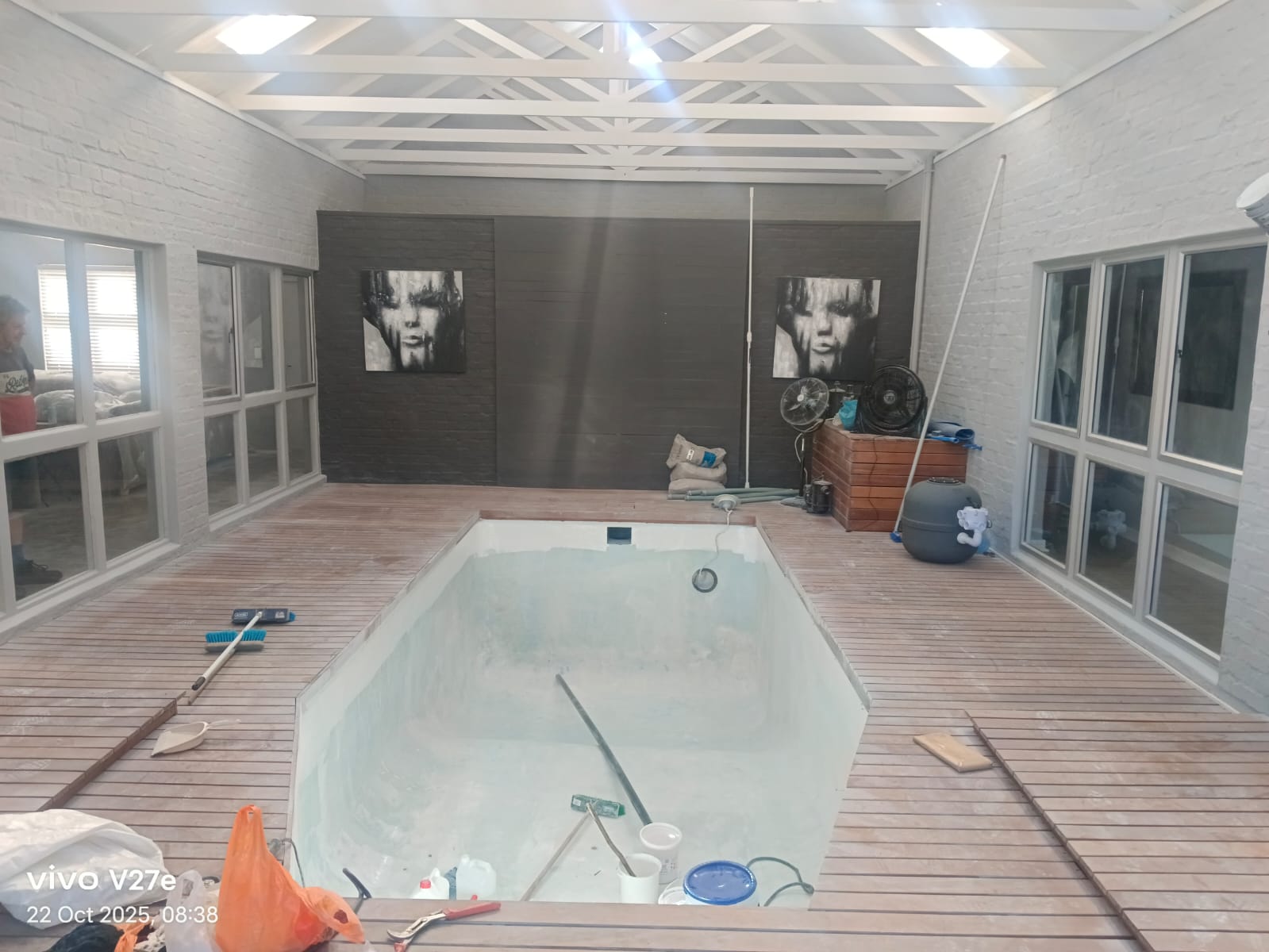 An indoor pool under a pitched roof being renovated, surrounded by a timber deck