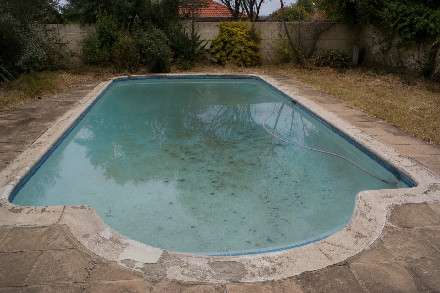 Neglected older swimming pool with stained patchy marbelite surface, cloudy water and worn coping needing repair