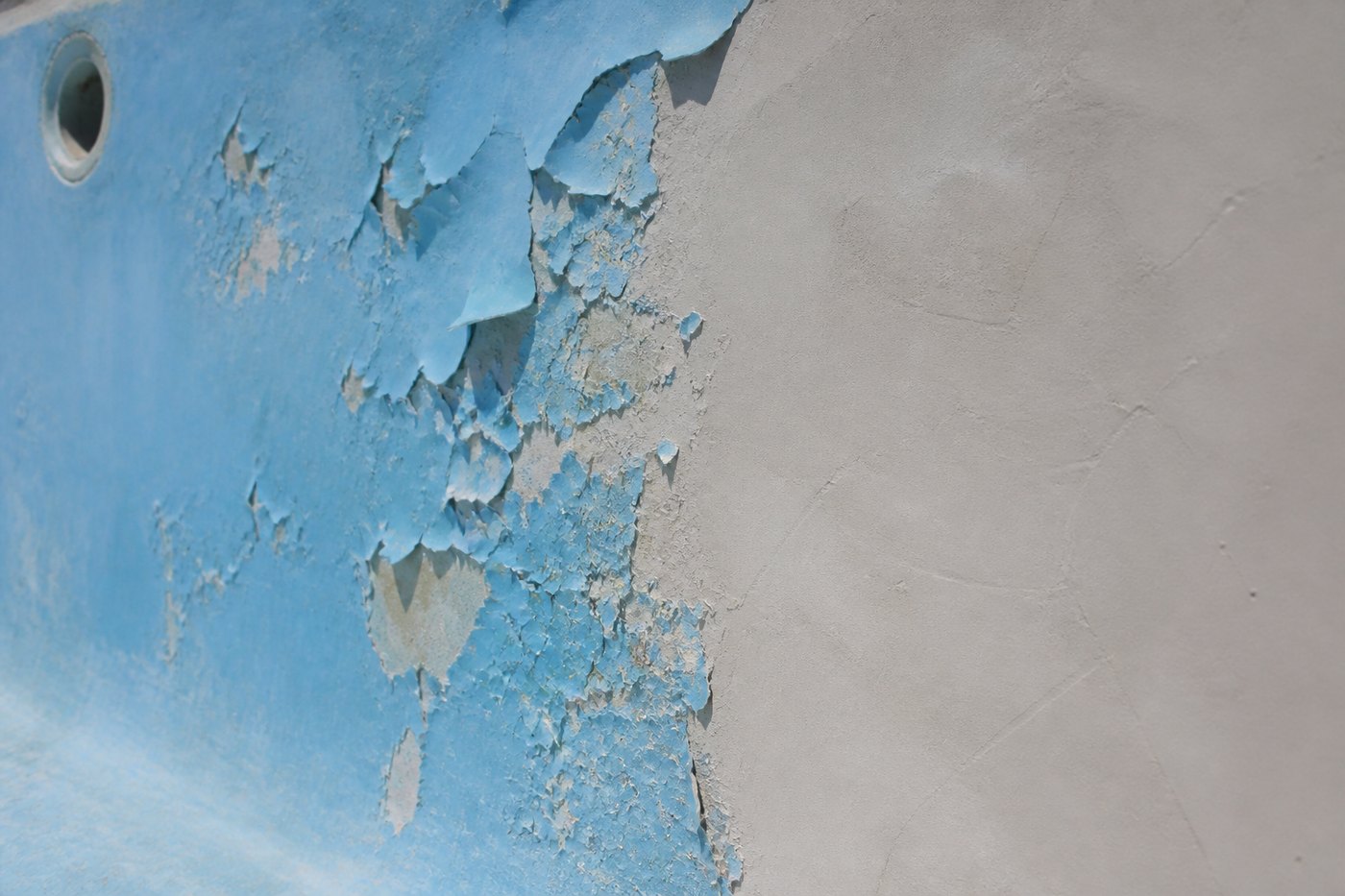 Empty pool wall with old blue pool paint peeling away on one side and clean prepared grey substrate on the other