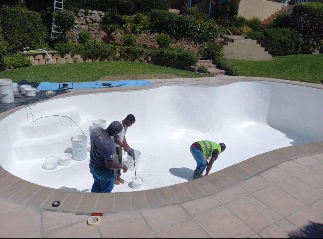 Three Kwik Pools technicians applying new white plaster to a large freeform pool in a sloped garden