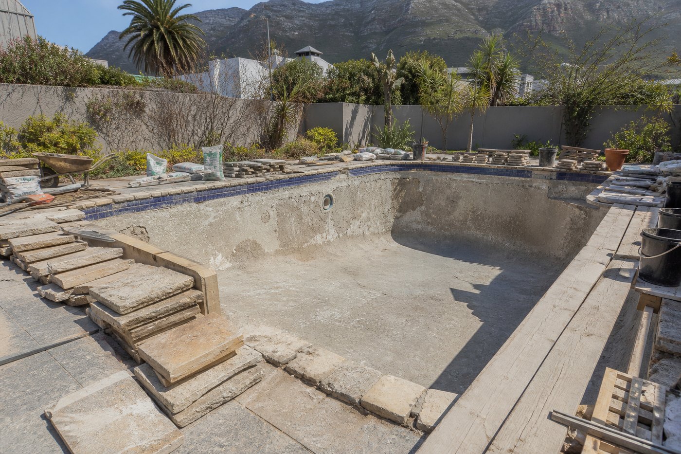 Drained Cape Town swimming pool mid renovation with the surface stripped back, coping lifted and building materials around the edge