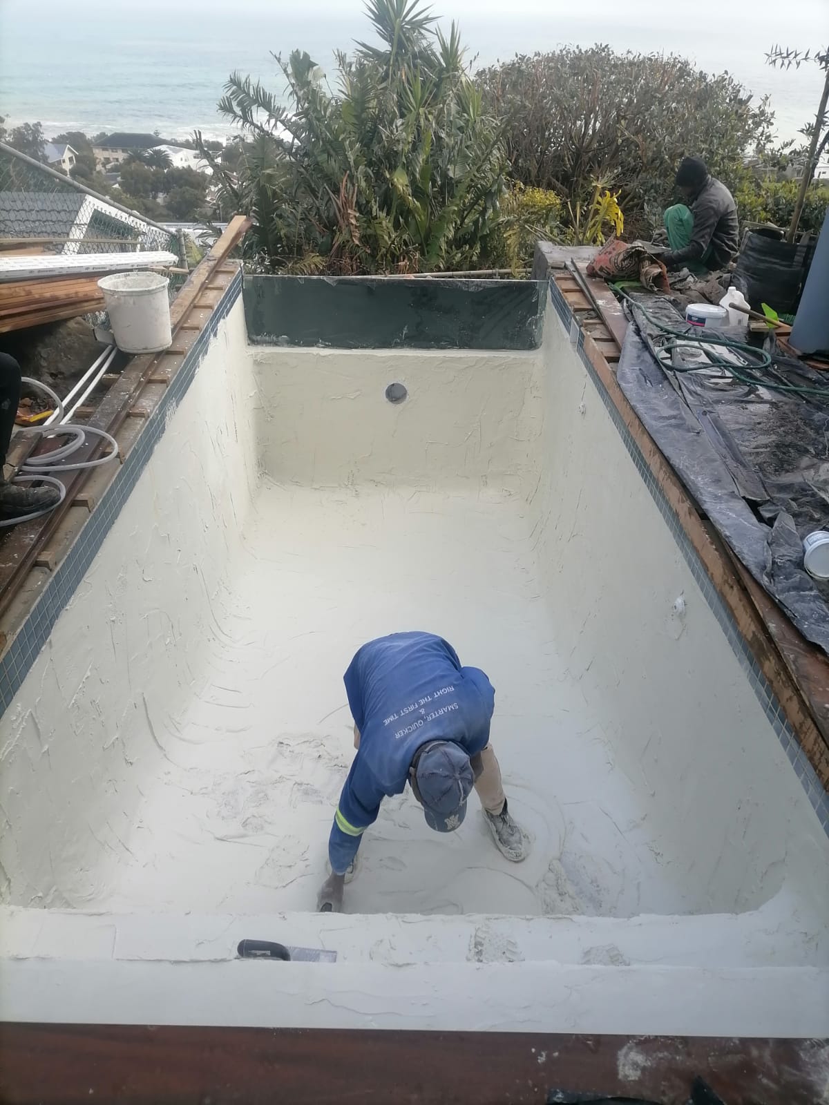 A Kwik Pools technician hand finishing a rectangular pool surface at a property overlooking the sea