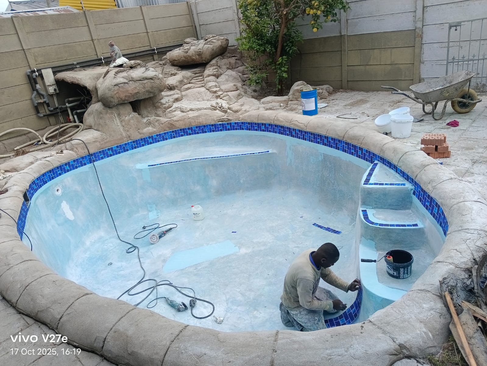 Kwik Pools technician laying new blue mosaic waterline tiles during a pool resurfacing in Cape Town