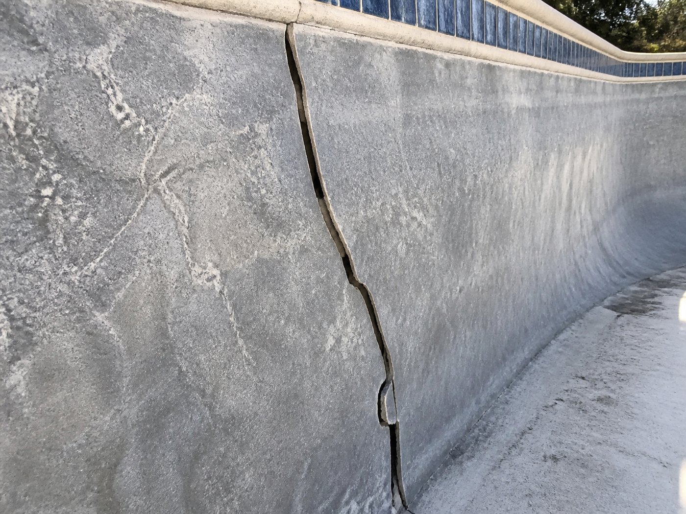Long structural crack running down the marbelite wall of an empty swimming pool with mosaic waterline tiles above